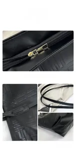 Detail of black tote bag showing geometric embossed texture and gold metal zipper hardware