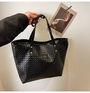 Detail of woven black tote bag featuring gold studs and leather FASHION label
