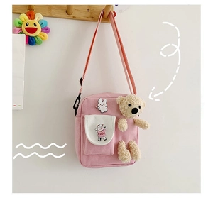 Détail d'un sac à bandoulière rose en toile avec poche vache dessinée et breloque ours peluche