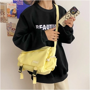 Detail view of yellow canvas messenger bag with fashion label and buckled flap closure
