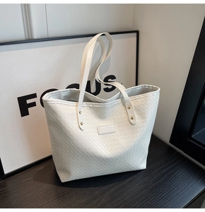 Detail of white woven tote bag featuring reinforced rivets and a fashion logo patch