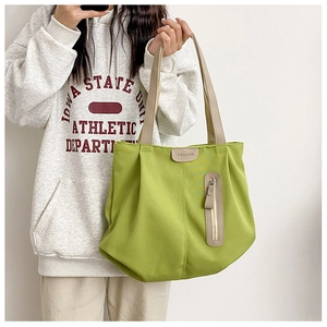 Detail view of bright green nylon tote bag with beige straps and fashion label decoration