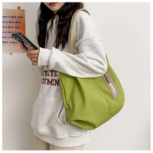 Detail view of large green canvas tote bag featuring beige straps and vertical zipper