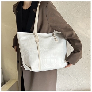 Detail of white tote bag with embossed checkerboard texture and beige leather handles