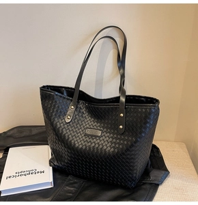 Detailed close-up of woven black tote bag featuring a gold rivet and fashion leather label