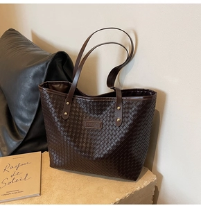 Close-up of dark brown woven leather tote bag with fashion tag and gold rivets