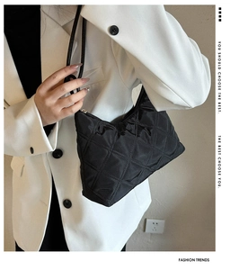 Detail of a black quilted shoulder bag worn with a white suit for a modern minimalist style
