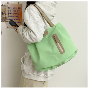 Detail view of light green tote bag showing side zip pocket and brown leather straps