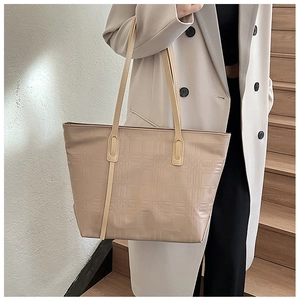 Detail shot of beige tote bag featuring classic geometric embossed grid texture and long straps