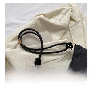 Close-up of black quilted handbag with knot strap detail and metal ring on white blazer
