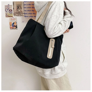 Detail of a black canvas tote bag with contrast cream straps and functional front zipper
