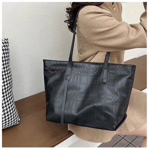 Detail of black tote bag featuring textured lattice embossed pattern and long shoulder straps
