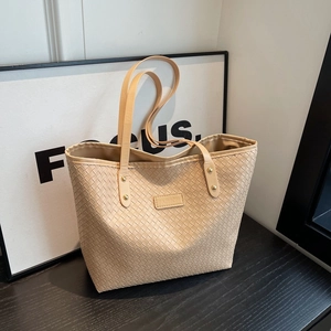 Beige woven tote bag with shoulder straps and fashion label in a modern indoor setting