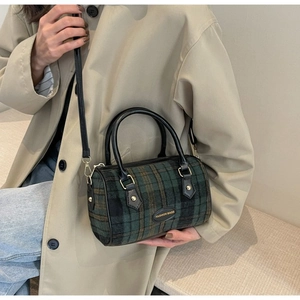 Close-up of a green and black plaid boston bag with leather handles and fashion bag logo