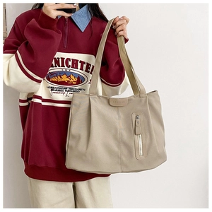 Detail of light beige canvas tote bag with front zip pocket and FASHION logo tag