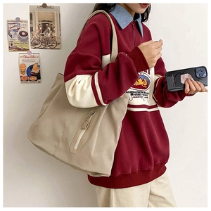 Detail of beige large capacity tote bag with vertical zipper shown on a shoulder