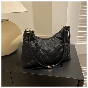 Detailed close-up of black quilted shoulder bag with gold metal rings and silk texture