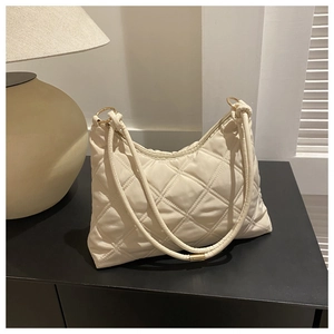 Close-up of quilted cream shoulder bag featuring gold rings and elegant dual straps