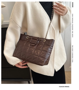 Detail of dark brown quilted leather crossbody bag with chain strap on a model