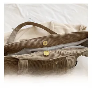 Detail of the golden magnetic closure and embroidery on the khaki corduroy tote bag
