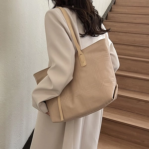 Minimalist beige tote bag with embossed lattice pattern shown on shoulder in a lifestyle setting