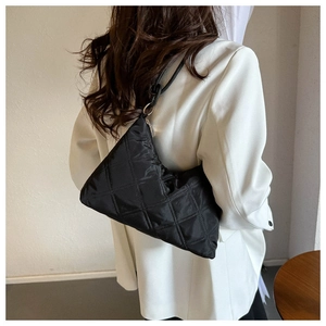 Detail view of black quilted crossbody bag worn by model in a white blazer