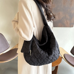 Detail of black tote bag featuring heart-shaped quilted pattern and golden zipper texture