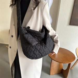 Detail of black heart-quilted puffer tote bag with matching small heart pouch on model