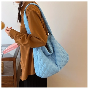 Sac fourre-tout matelassé bleu clair porté à l'épaule dans un décor intérieur épuré