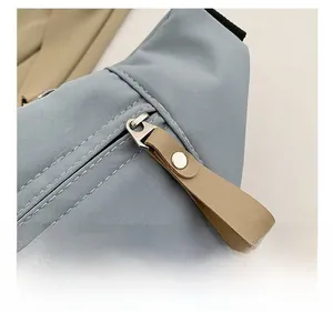 Dettaglio macro della cerniera argentata e tirante in pelle kaki sulla borsa in nylon