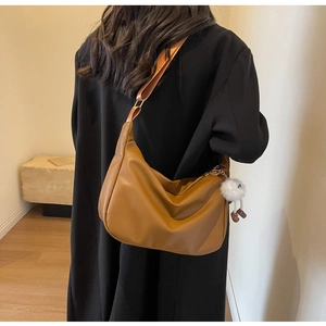 Détail d'un sac à bandoulière en cuir grainé marron avec pompon blanc et sangle large