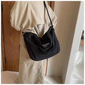 Detail of black corduroy tote bag showing fine ribbed texture and embroidered logo label