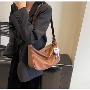Sac hobo marron en cuir avec charm en peluche porté sur un blazer noir élégant