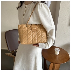 Detail of khaki quilted tote bag with gold chain strap worn in elegant cafe setting