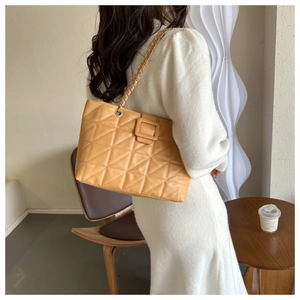 Detail view of quilted yellow tote bag with chain strap on model in a cozy interior