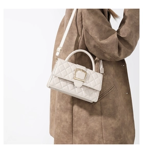 Détail d'un sac à bandoulière matelassé beige avec boucle dorée et poignée rigide