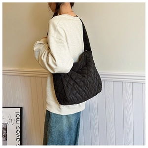 Détail latéral d'un grand sac cabas noir matelassé avec motif losanges porté par un modèle