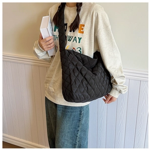 Détail du sac à bandoulière noir matelassé porté par un mannequin sur fond blanc minimaliste
