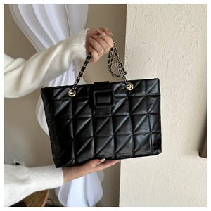 Close-up of black quilted tote bag featuring a square buckle and gold metal chain handles