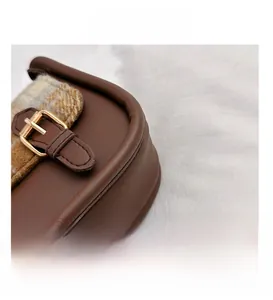 Detailaufnahme von braunem Leder, Karo-Stoff-Nähten und goldener Metallschnalle der Tasche