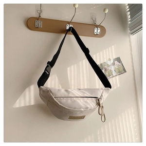 Dettaglio di una borsa a tracolla in nylon beige appesa a un gancio con patch moda