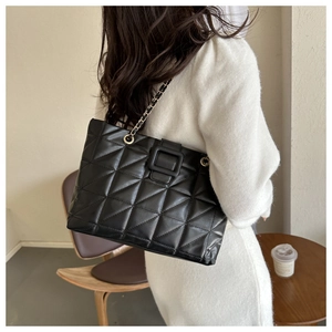 Close-up of black quilted tote bag with chain strap worn by a model in a cafe