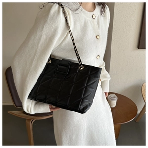 Detail of black quilted leather shoulder bag featuring large square buckle and chain strap
