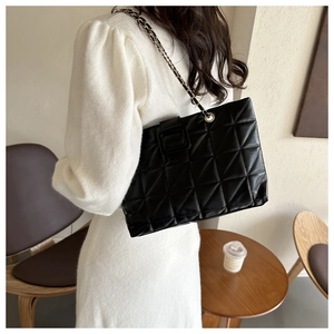Detail of black quilted tote bag with metallic chain strap on shoulder in cafe setting