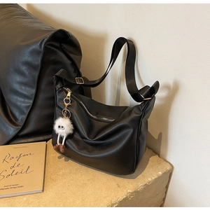 Gros plan d'un sac hobo en cuir noir avec motif litchi et porte-clés en peluche blanc