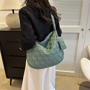 Green quilted tote bag with heart embroidery shown on shoulder in minimalist interior