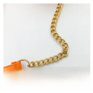 Close-up of bright orange leather strap and light gold metal chain detail for handbag