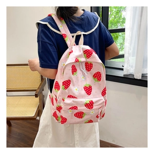Pink student backpack with strawberry and daisy prints worn by a model in a cozy room