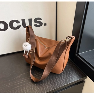 Gros plan du sac bandoulière en cuir marron avec large sangle et breloque en peluche