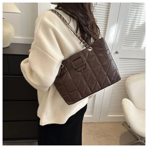 Detail view of coffee brown quilted tote bag with golden chain strap on model